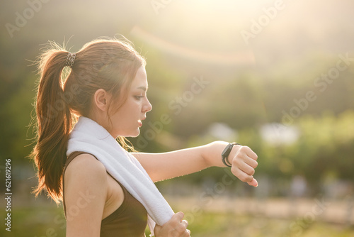 Healthy woman relax after cool down and looking smart watch for check timing run. Woman workout after fitness and jogging session at the park. Healthy and Lifestyle Concept.