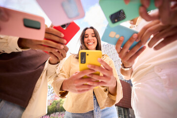 Caucasian girl looking at happy cell phone. Low angle view of group friends addicted to technology. People gathered in circle using mobile. New generations and communication through social networks.