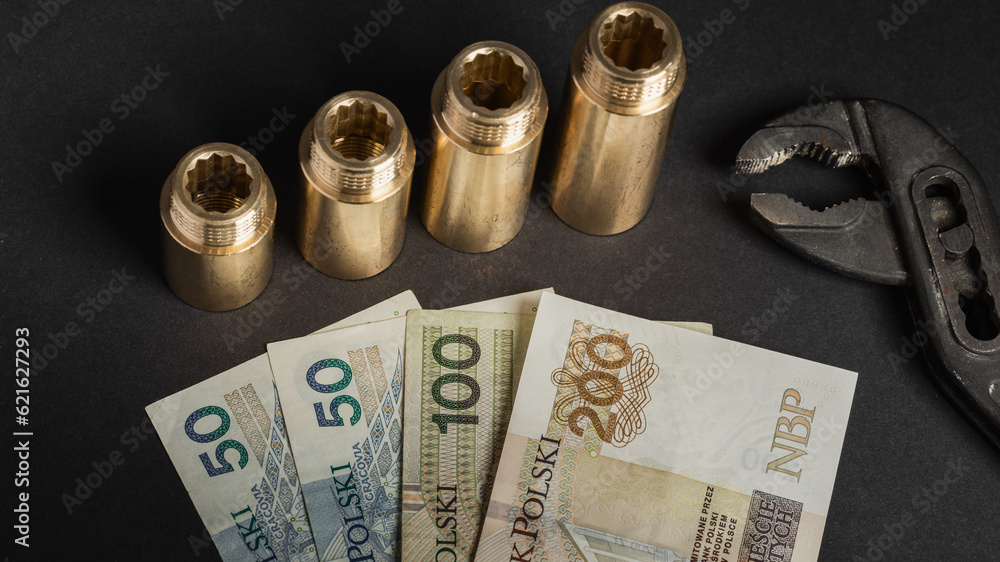 warsaw, poland - 07 07 2023: Polish banknotes of PLN on a black background, next to the brass hydraulic connectors and the key tool (selective focus) warsaw, poland - 07 07 2023: Polish banknotes of PLN on a black background, next to the brass hydraulic connectors and the key tool (selective focus)