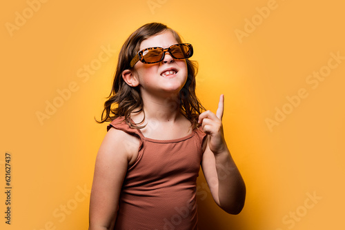 Delighted little kid in summer outfit pointing up in orange studio photo