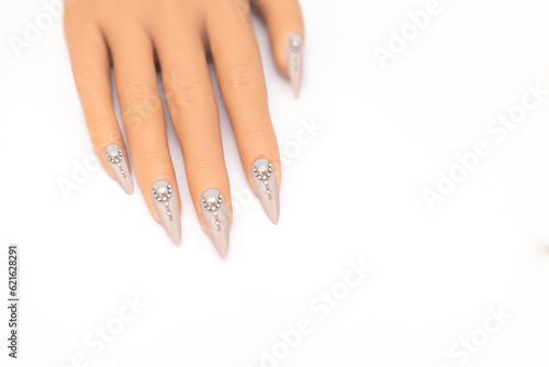 Female hand with long nails with glitter nail polish. Long gray nail design with rhinestones. Women hand with sparkle manicure on white background photo