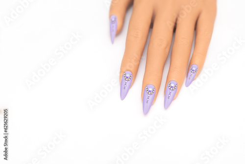 Female hand with long nails with glitter nail polish. Long purple nail design with rhinestones. Women hand with sparkle manicure on white background photo