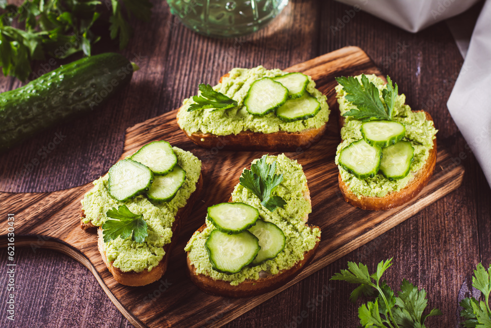 Crostini with avocado puree, cucumbers and herbs on a wooden board Crostini with avocado puree, cucumbers and herbs on a wooden board