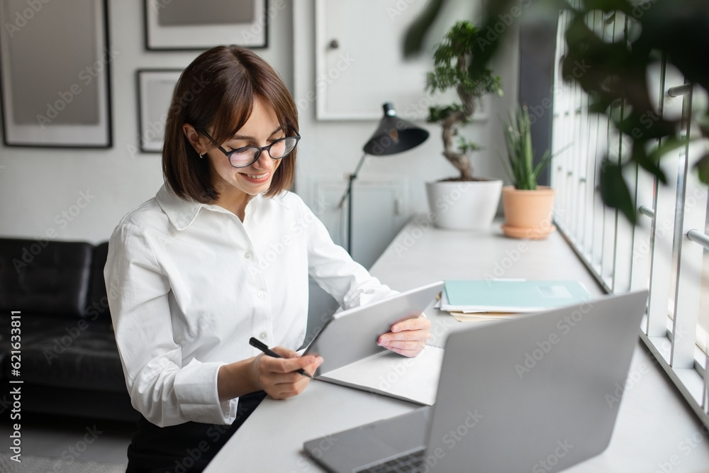 Happy businesswoman using digital tablet at workplace in office, reading emails or browsing new business application Happy businesswoman using digital tablet at workplace in office, reading emails or browsing new business application