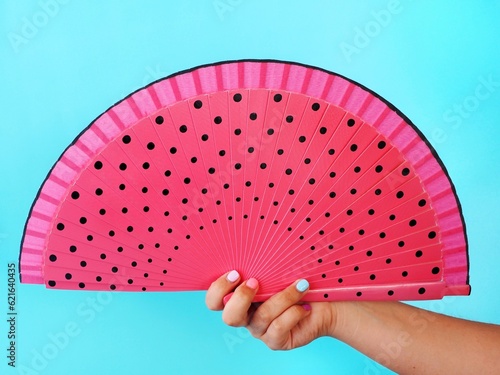A hand holding a hand fan with black dots 