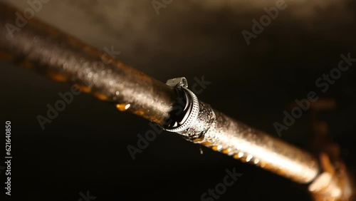 A male plumber puts a metal clamp on a water pipe. A man in the basement, repairing a water pipe from leaking.