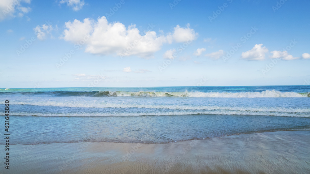 Golden sand and blue ocean water with white clouds. Karon Beach. In places, high waves and splashes. Blue sky. The sun's rays are reflected on the sand. White foam from the waves. Thailand