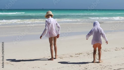 Children play on the sandy beach on a hot sunny day.A boy and a girl are writing something in the sand with their foot.Brother and sister play together on the seashore.The concept of family holidays