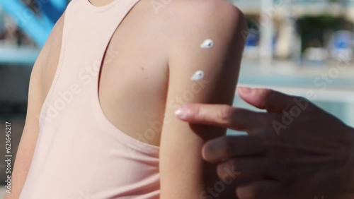 Mom applies and rubs sunscreen on her daughter's shoulder and arm in close-up.Protection of children on a sunny day.Family vacation on the beach.Applying sunscreen