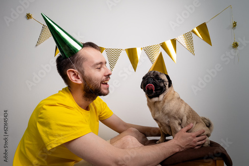 Photography Caucasian man owner congratulation cute funny pug dog with pet birthday in a party hat