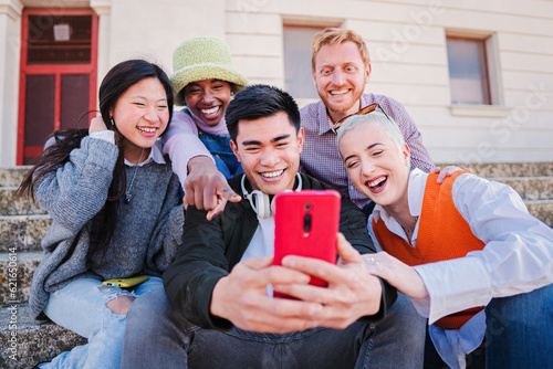 Group of multiracial best firends faving fun using a smartphone. Young people smiling and watching the social media app on a cellphone. Happy buddies browsing online on internet with a mobile phone photo