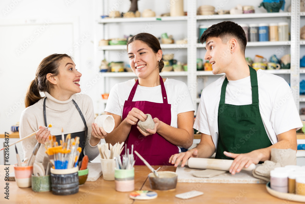 Fototapeta premium Two young women and young man sculpt pottery in workshop