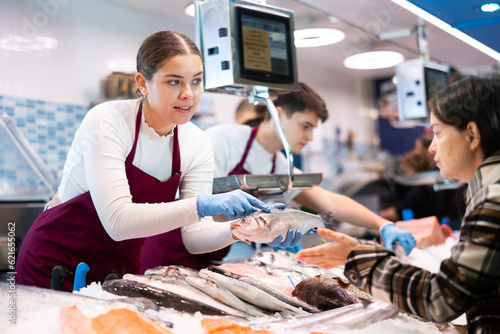 Photos Female seller in apron standing near counter offering fresh fish hake to the buy