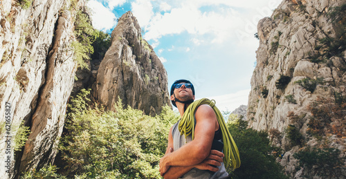 Valokuva Portrait of smiling climber man in protective helmet and sunglasses with climbing rope on the shoulder standing in Paklenica park between rock cliff walls