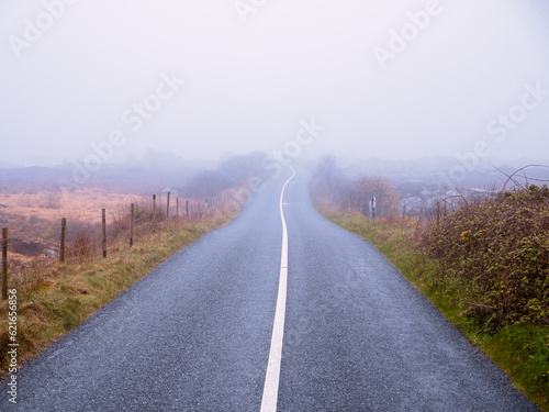 Asphalt road and fields in country side in a fog. Dangerous driving conditions with low visibility and wet road surface. Mist over wild nature. Irish country side. © mark_gusev