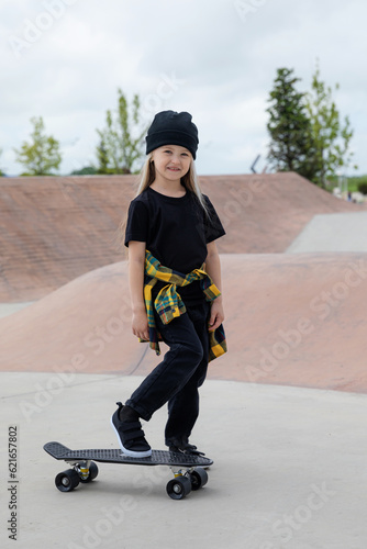 Pretty happy little girl riding on skateboard in skate park in summer day