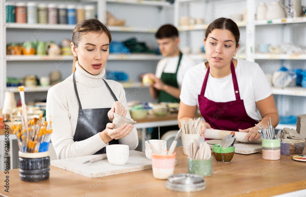 Fototapeta premium Two young women in apron modeling clay pottery in workshop