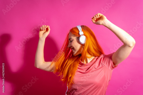 Redhead woman in studio photography dancing on a pink background, in hard light