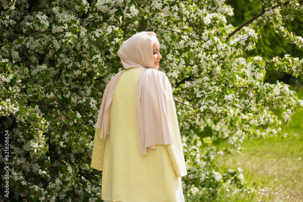 Portrait of A young Muslim woman in a white dress and yellow jacket in front of a flowering tree. close plan. Blooming apple tree. Pretty modest Muslim woman. European Muslim. tenderness. close plan. Portrait of A young Muslim woman in a white dress and yellow jacket in front of a flowering tree. close plan. Blooming apple tree. Pretty modest Muslim woman. European Muslim. tenderness. close plan.