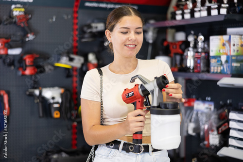 Smiling young woman involved in crafts or hobbies using of paint, choosing air sprayer in local hardware store