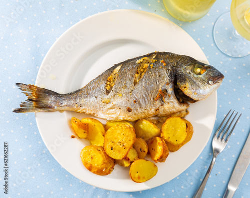 Delicious baked fish called Dorada with toasted potatoes cut in half photo