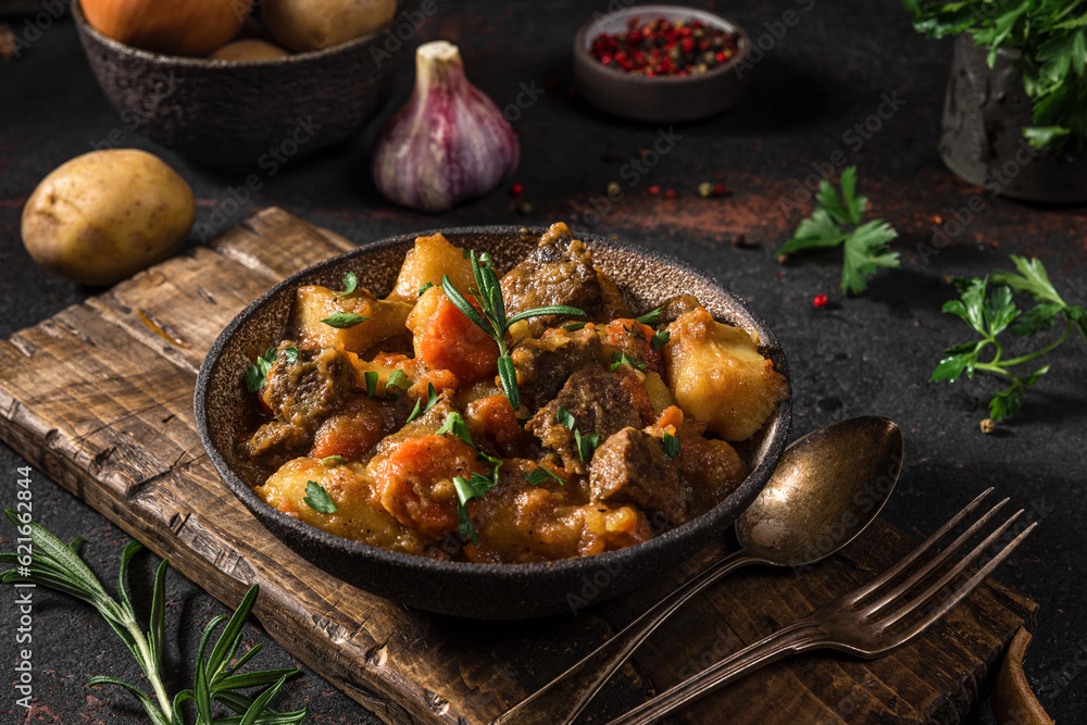 Irish stew made with beef, potatoes, carrots and herbs in a plate with cutlery on black background Irish stew made with beef, potatoes, carrots and herbs in a plate with cutlery on black background