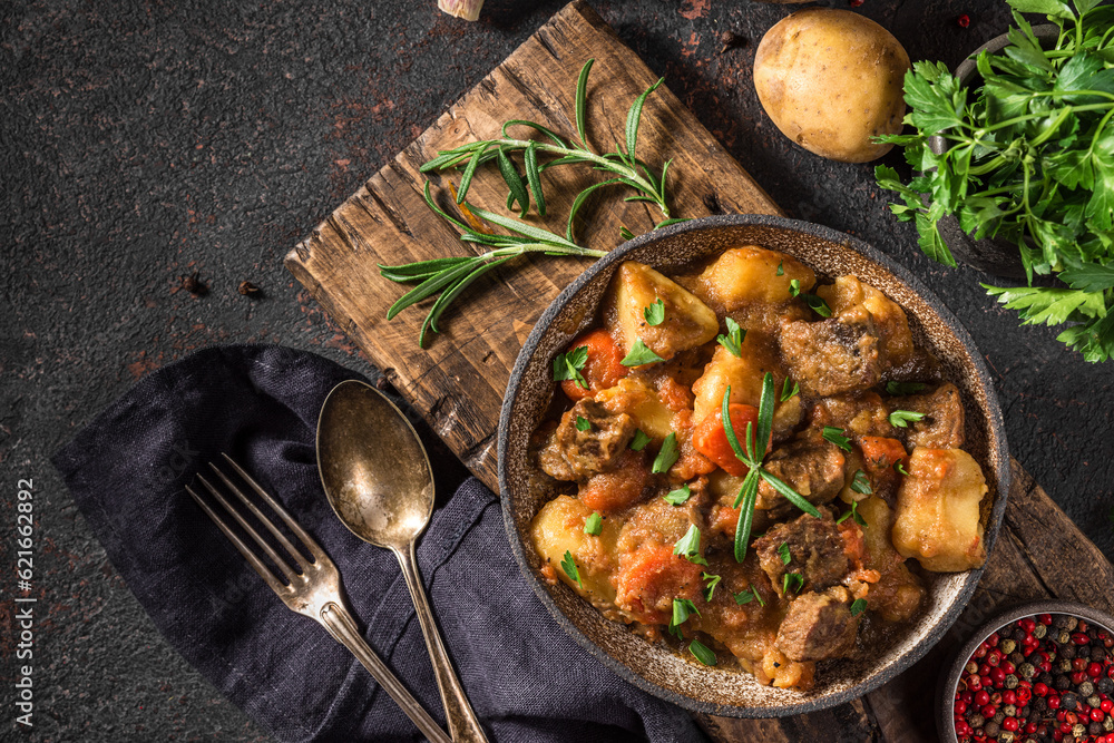 Beef meat stewed with potatoes, herbs and carrots in a plate with a spoon on black background. top view Beef meat stewed with potatoes, herbs and carrots in a plate with a spoon on black background. top view