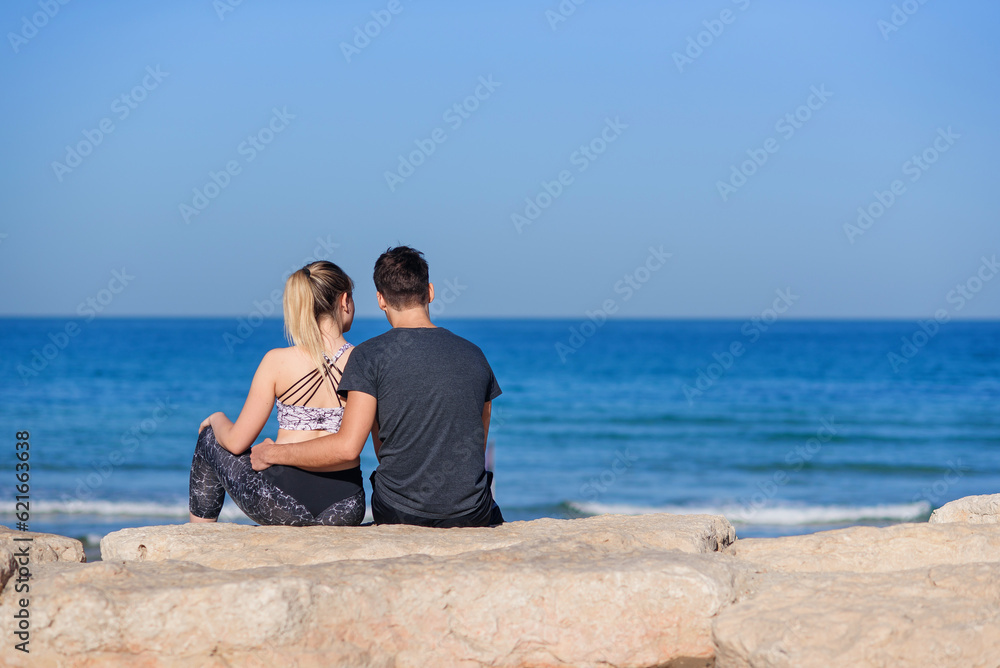 Young couple in love sitting on the rocky beach and looking on the horizon at sea.