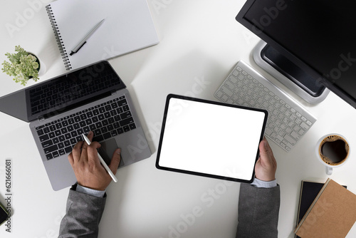 A young businessman is working on the laptop using a desktop computer with a blank screen and an empty copy space display.