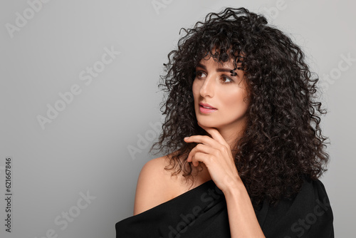 Beautiful young woman with long curly hair on light grey background. Space for text