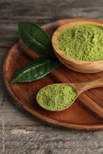 Spoon and bowl with green matcha powder on wooden table, closeup