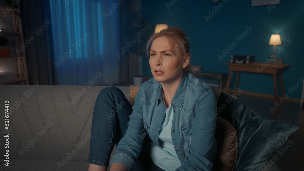 A young woman sits on a sofa with legs and watches TV in the evening. A woman watches a movie, a reality show, listens carefully, is surprised by the plot twist. Portrait of a surprised woman close up A young woman sits on a sofa with legs and watches TV in the evening. A woman watches a movie, a reality show, listens carefully, is surprised by the plot twist. Portrait of a surprised woman close up