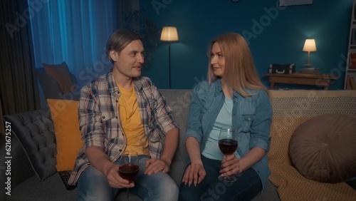 Young people are sitting on the sofa with glasses of red wine in their hands. The couple talks, spends a pleasant evening together.