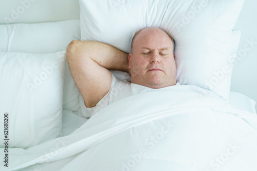 Caucasian white oversize body - fat man sleeping on the bed in bedroom close up. Health care and wellbeing concept.