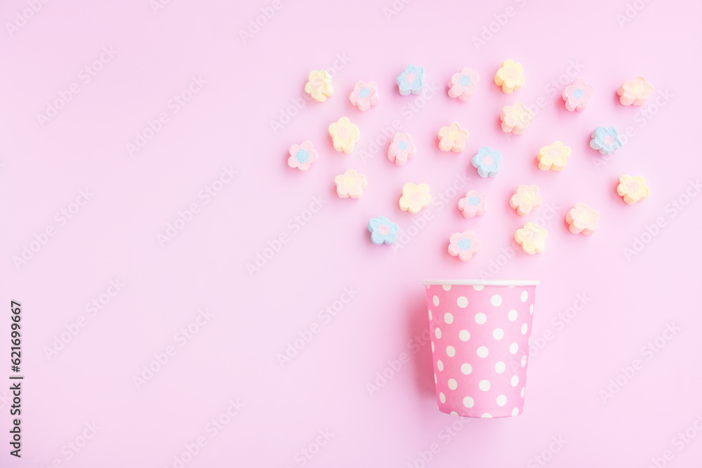 Flower Shaped Marshmallows out of a pink paper cup with white dot on pink background, Multicolored Marshmallows Flower Shaped Marshmallows out of a pink paper cup with white dot on pink background, Multicolored Marshmallows