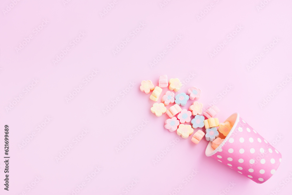 Flower Shaped Marshmallows out of a pink paper cup with white dot on pink background, Multicolored Marshmallows Flower Shaped Marshmallows out of a pink paper cup with white dot on pink background, Multicolored Marshmallows
