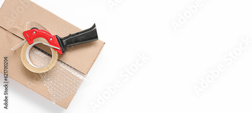 Packing tape dispenser, cardboard box and bubble wrap on white background with space for text photo