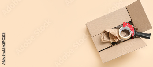 Fotografija Packing tape dispenser, cardboard box and wrapping paper on beige background wit