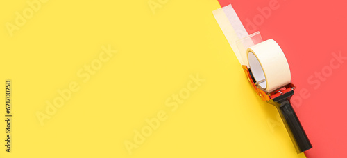 Packing tape dispenser on red and yellow background with space for text photo