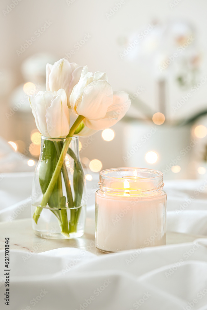 Burning candle and vase with tulips on bed, closeup