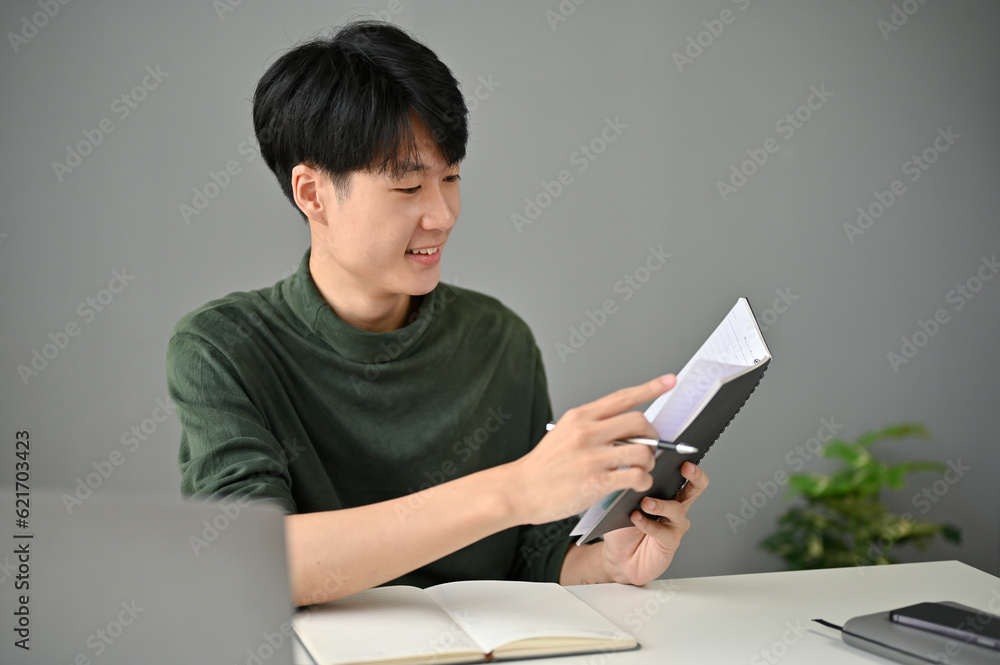 A handsome Asian man checks his meeting schedules while working at his desk. A handsome Asian man checks his meeting schedules while working at his desk.