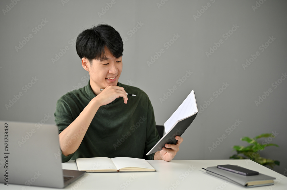 A handsome Asian man checks his meeting schedules in his personal planner book A handsome Asian man checks his meeting schedules in his personal planner book