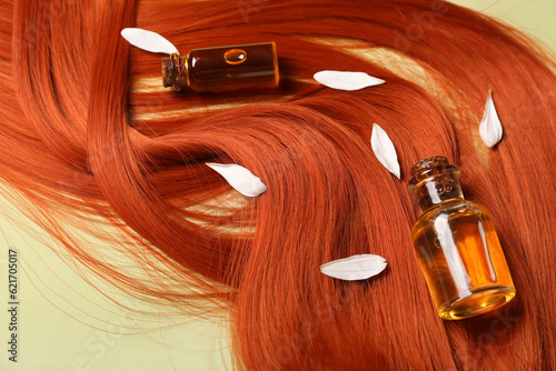 Composition with ginger hair strand, bottles of essential oil and flower petals on green background, closeup
