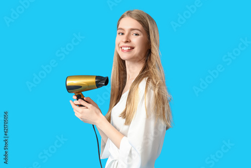 Young blonde woman with hair dryer on blue background