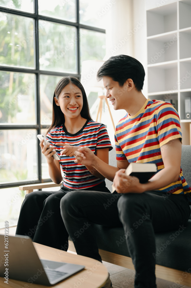 Two asian students learning together online with a laptop, tablet and tutor together in living room .