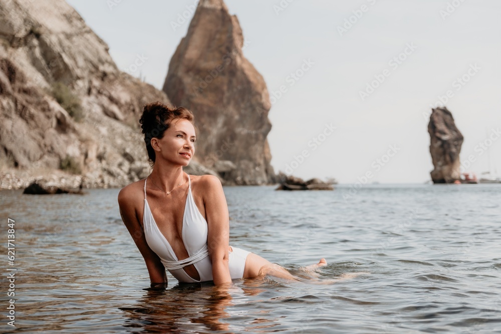 Woman sea fitness. Happy woman in a white bikini performing pilates in the sea on the beach. Female fitness yoga routine concept. Healthy lifestyle.