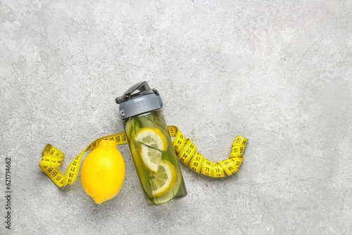 Sports bottle of lemonade with cucumber and measuring tape on white background