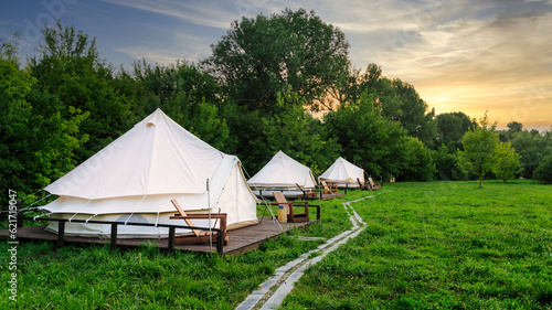 Glamping tents in nature with green grass at sunset. Summer season