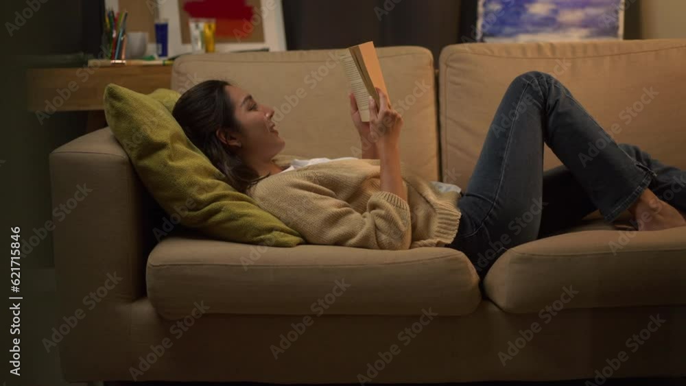 Happy woman opening, reading and relaxing a book on relax time at home. Vacation time of female reading a book on sofa at night. Education concept. Happy woman opening, reading and relaxing a book on relax time at home. Vacation time of female reading a book on sofa at night. Education concept.