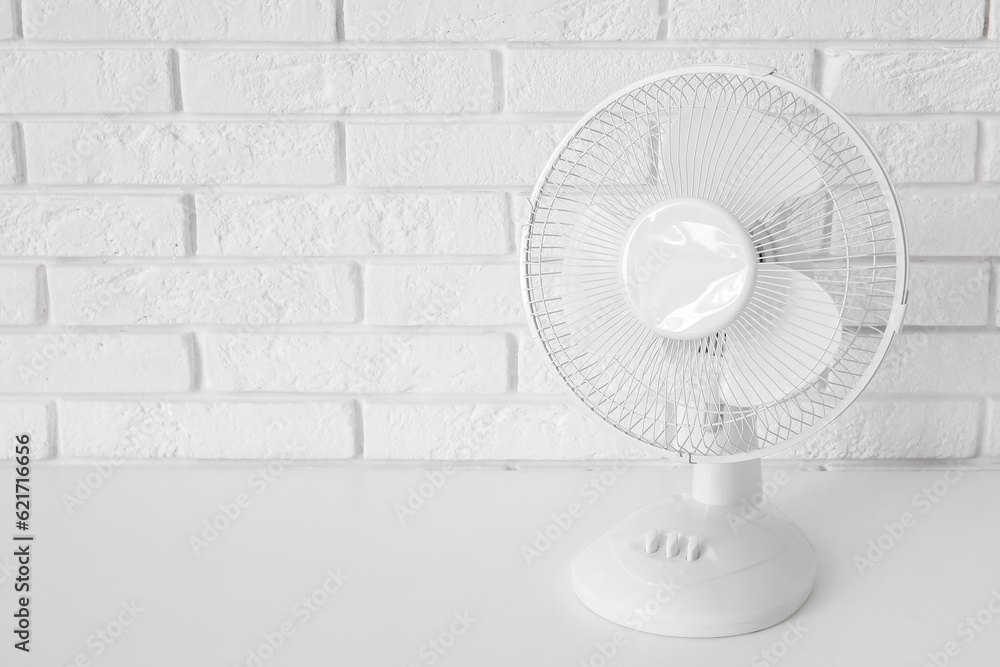 Table with modern electric fan near white brick wall
